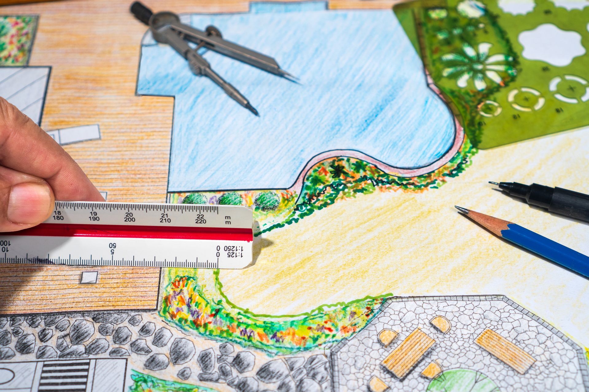 Des mains dessinent un plan de jardin coloré à l'aide d'une règle, d'un compas et d'un crayon sur du papier.