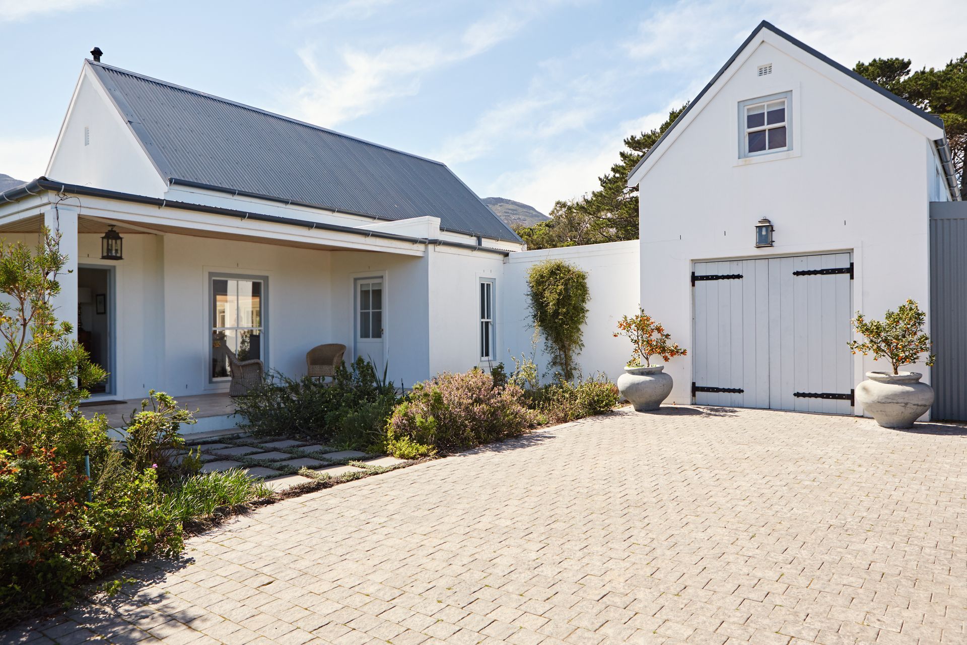 Maison blanche au toit foncé, garage indépendant et allée paysagée par une journée ensoleillée.