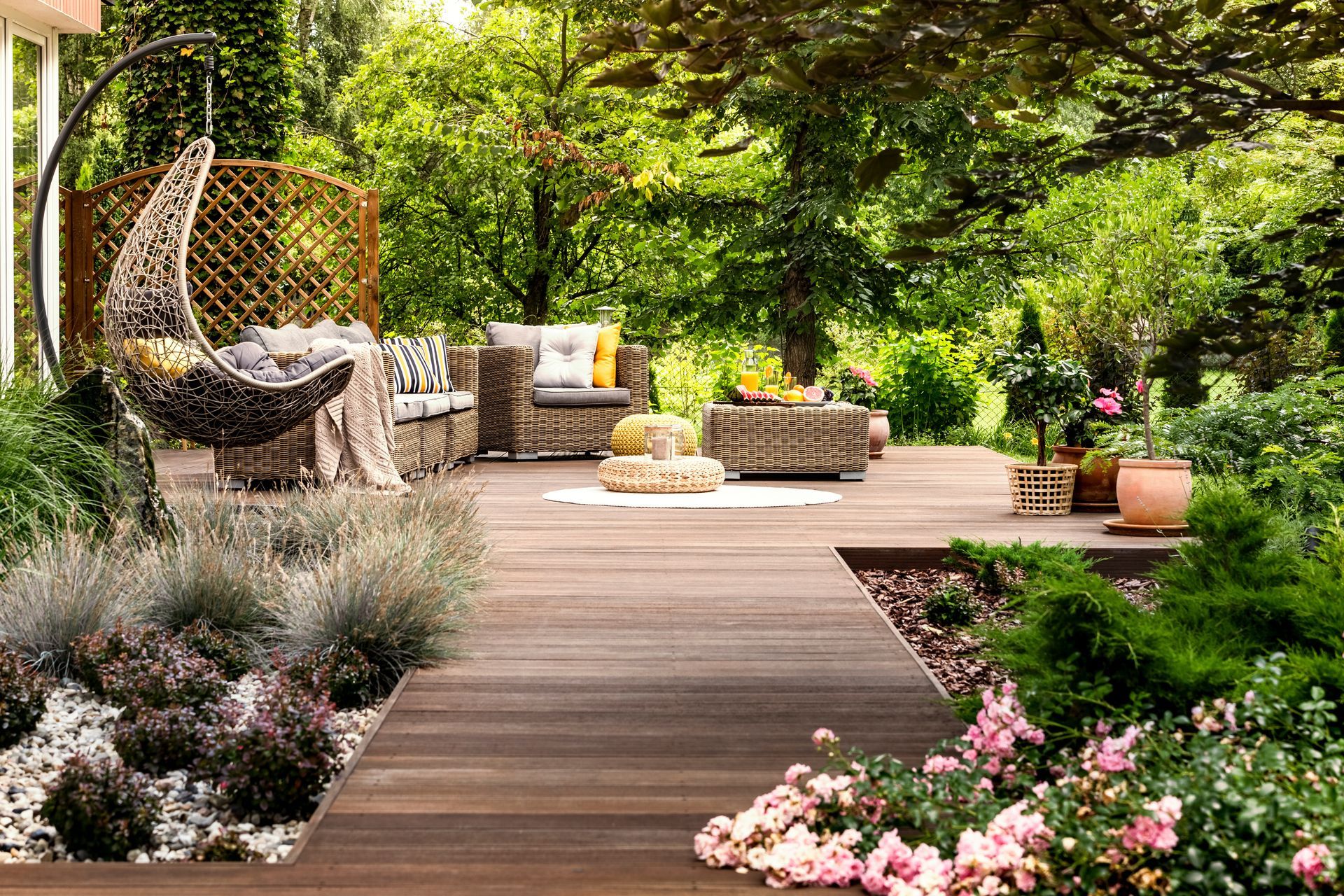 Terrasse de jardin en bois incurvée avec chaises longues en osier, coussins et une végétation luxuriante et des fleurs tout autour.