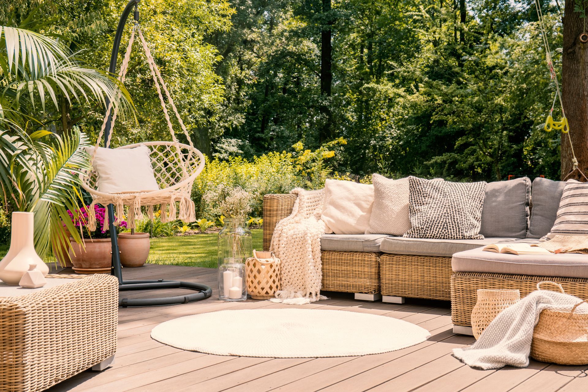 Patio extérieur confortable avec canapé en osier, table ronde, fauteuil suspendu et jardin luxuriant en arrière-plan.