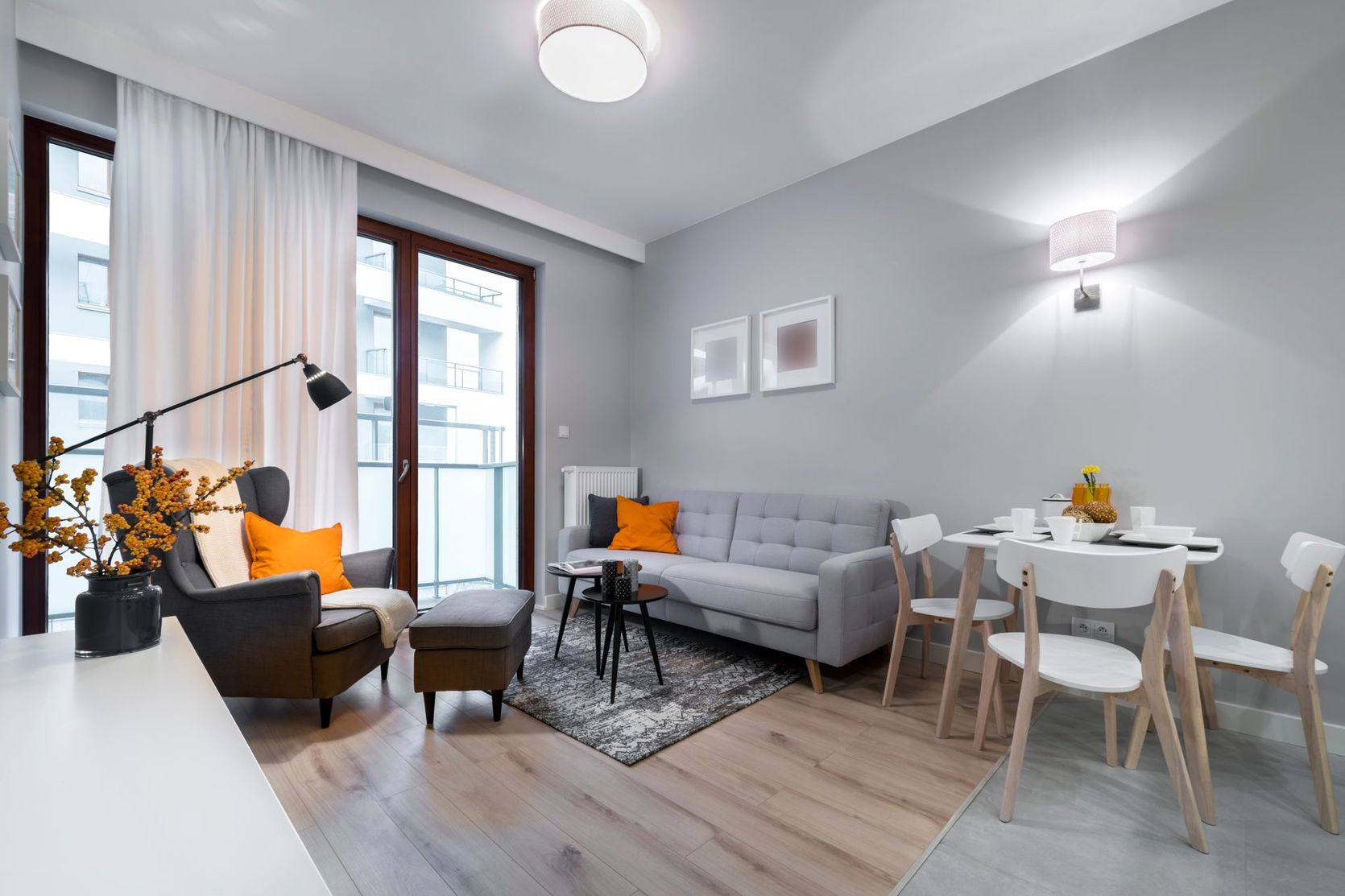 Salon moderne avec un canapé, un fauteuil, une salle à manger et des portes-fenêtres donnant sur un balcon.