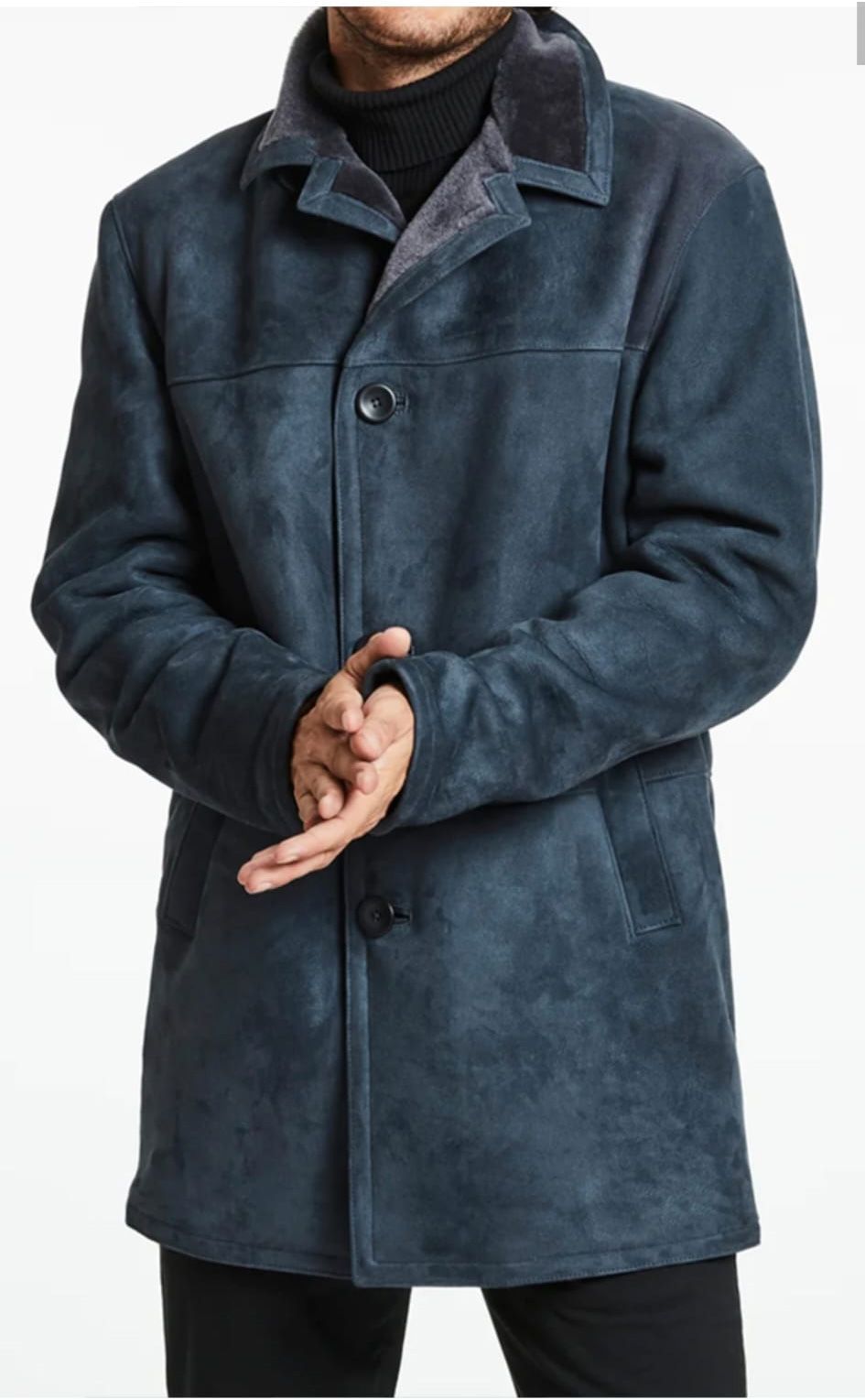 Hombre que lleva un abrigo azul oscuro, tipo gamuza, con cuello de piel y con las manos entrelazadas.