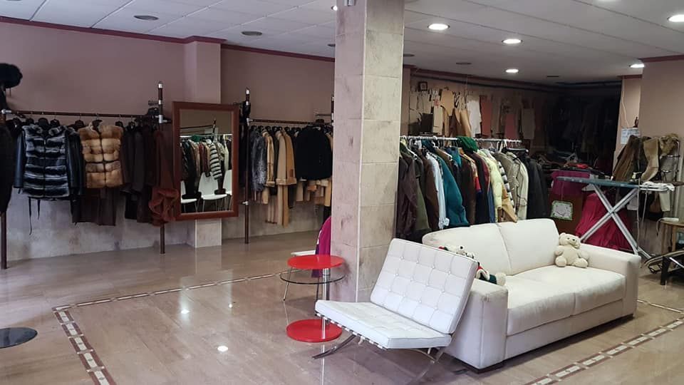 Interior de una tienda de ropa con percheros de abrigos y un sofá blanco.