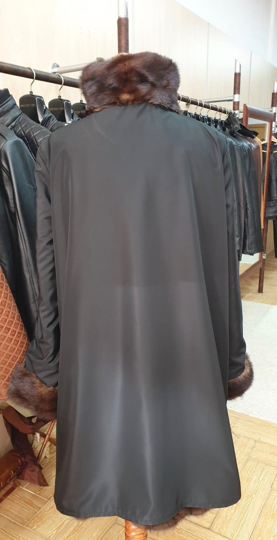 Abrigo negro con cuello y puños de piel sobre un maniquí, perchero al fondo.
