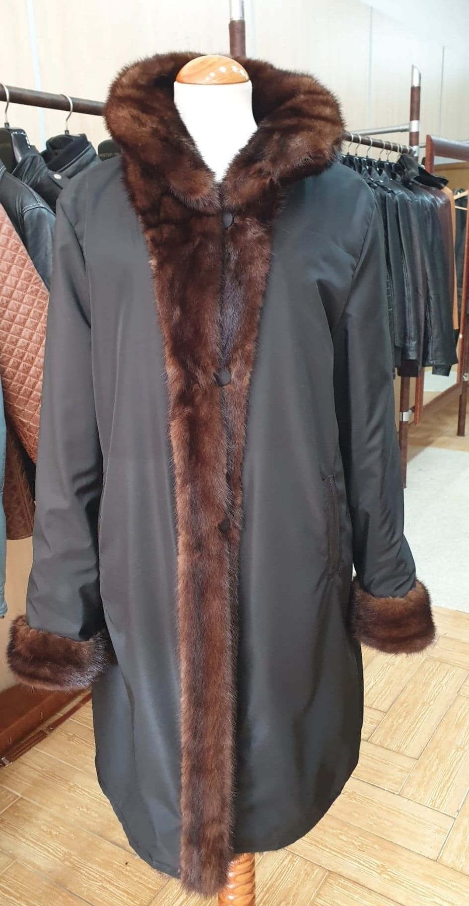 Abrigo negro con ribete de piel marrón y capucha expuesto en un maniquí.