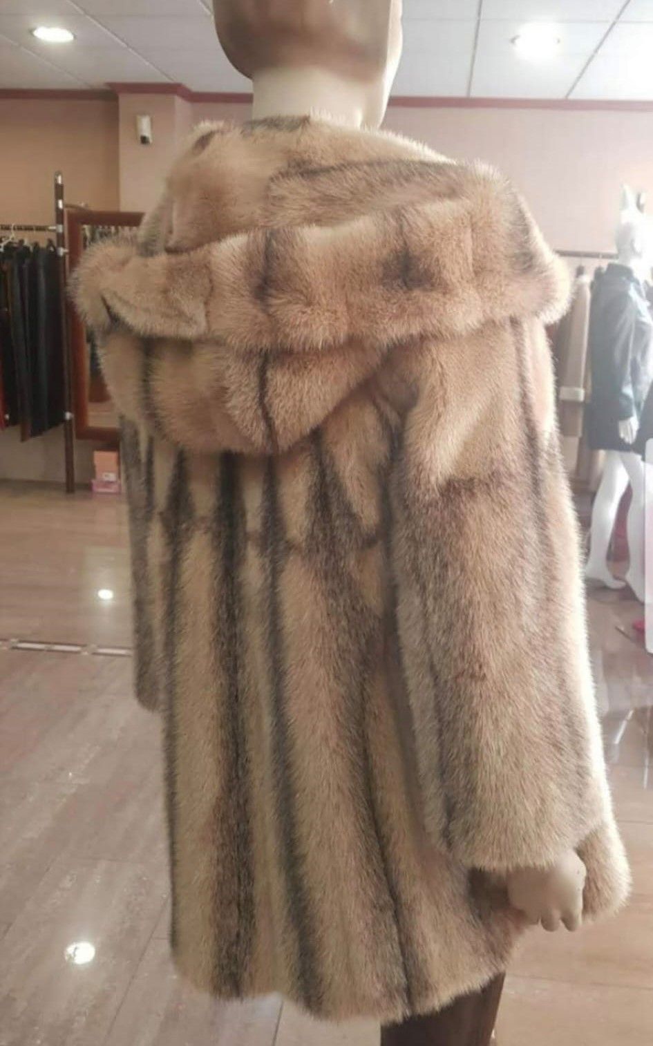 Maniquí con un abrigo largo de piel marrón claro con capucha; de pie en una tienda.