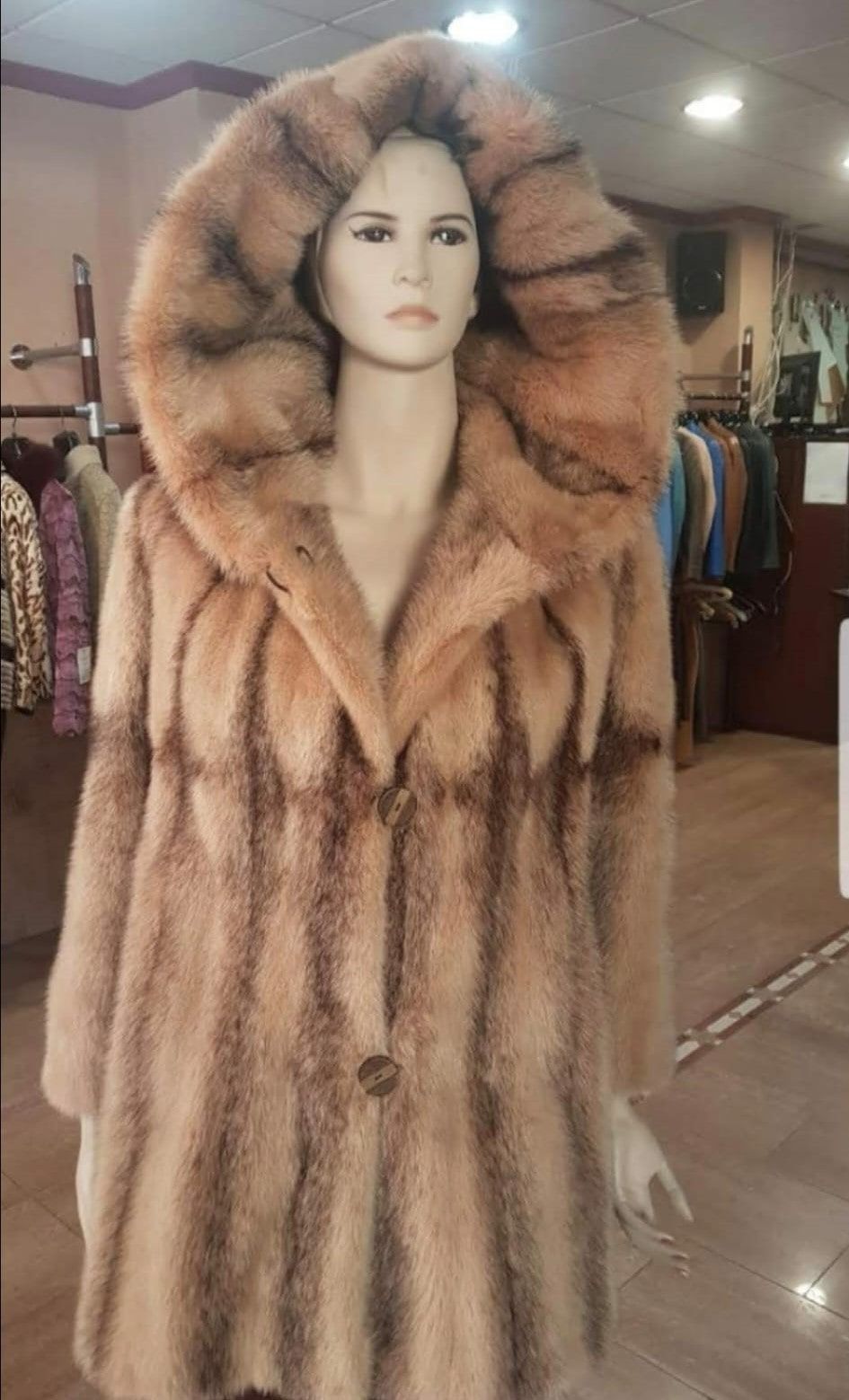 Maniquí con un abrigo largo de piel marrón con un gran cuello con capucha en una tienda de ropa.