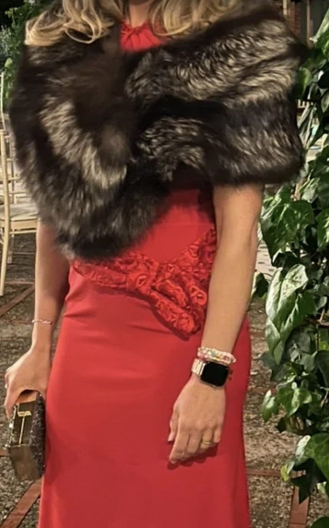 Mujer con vestido rojo y chal de piel, sosteniendo un bolso de mano.