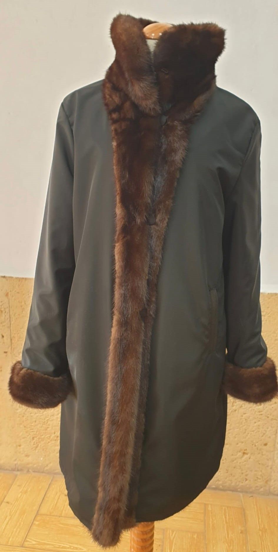 Abrigo negro con ribete de piel marrón sobre un maniquí de madera.