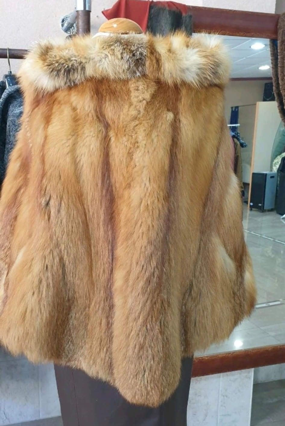 Una capa de piel marrón rojiza con capucha forrada de piel, exhibida en un maniquí en una tienda de ropa.