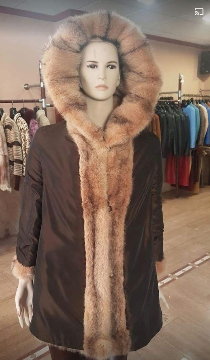 Maniquí con un abrigo oscuro con una gran capucha forrada de piel y panel central, en una tienda.