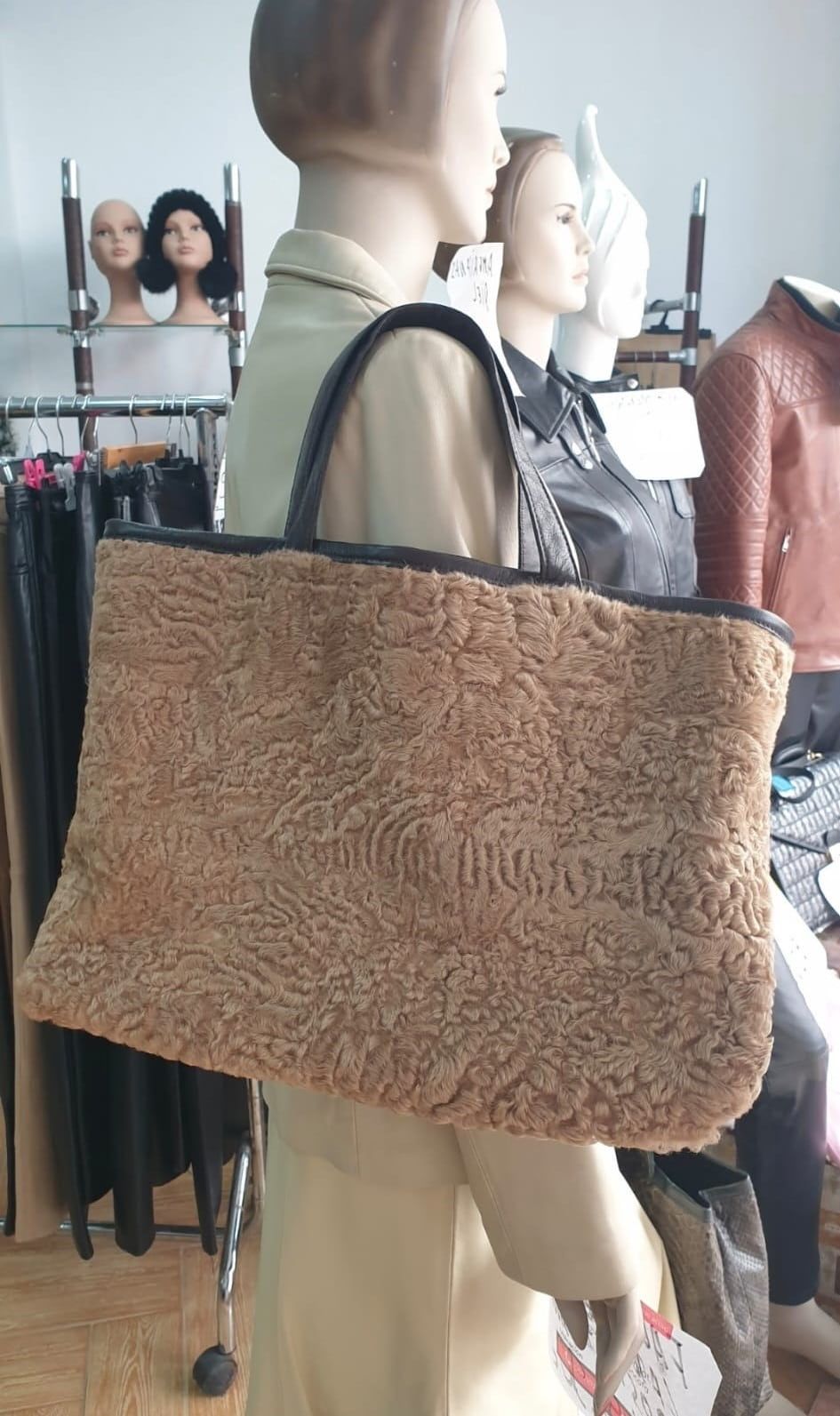 Bolso tote de pelo color canela con asas negras sobre un maniquí en una tienda de ropa.