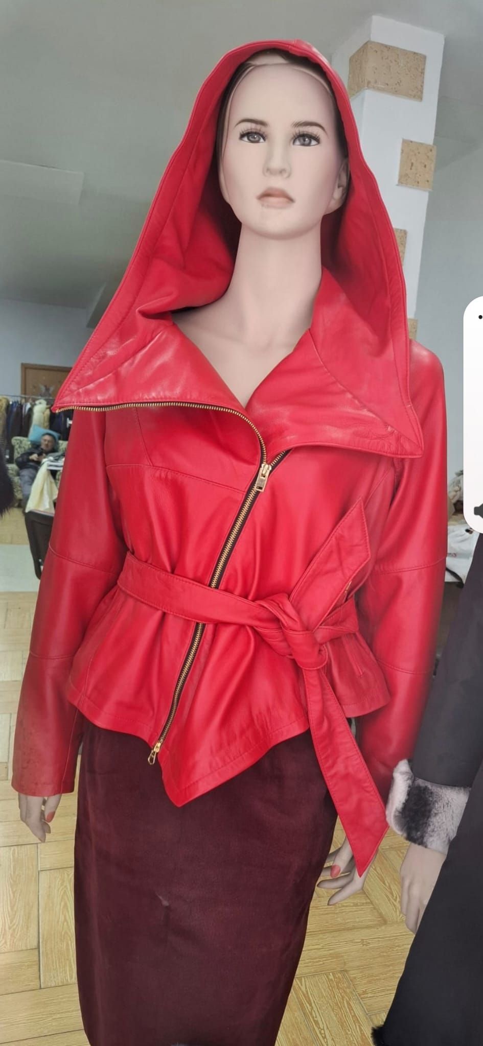 Maniquí con chaqueta de cuero roja, capucha y cinturón a juego. También lleva una falda burdeos oscura.