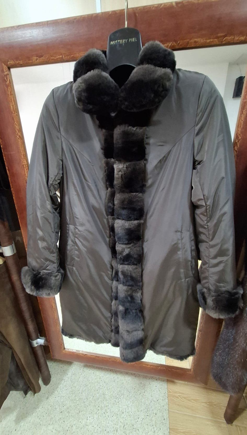 Abrigo marrón oscuro con ribete de piel, colgado en el interior de una tienda.