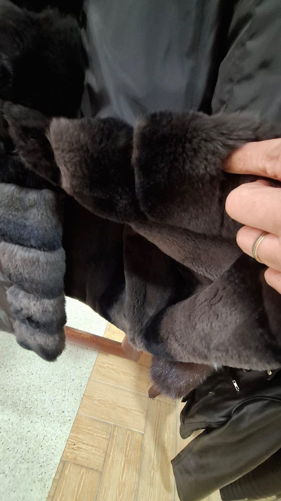 Primer plano del interior de un abrigo de piel oscura, que revela la textura del forro. Una mano toca la piel.