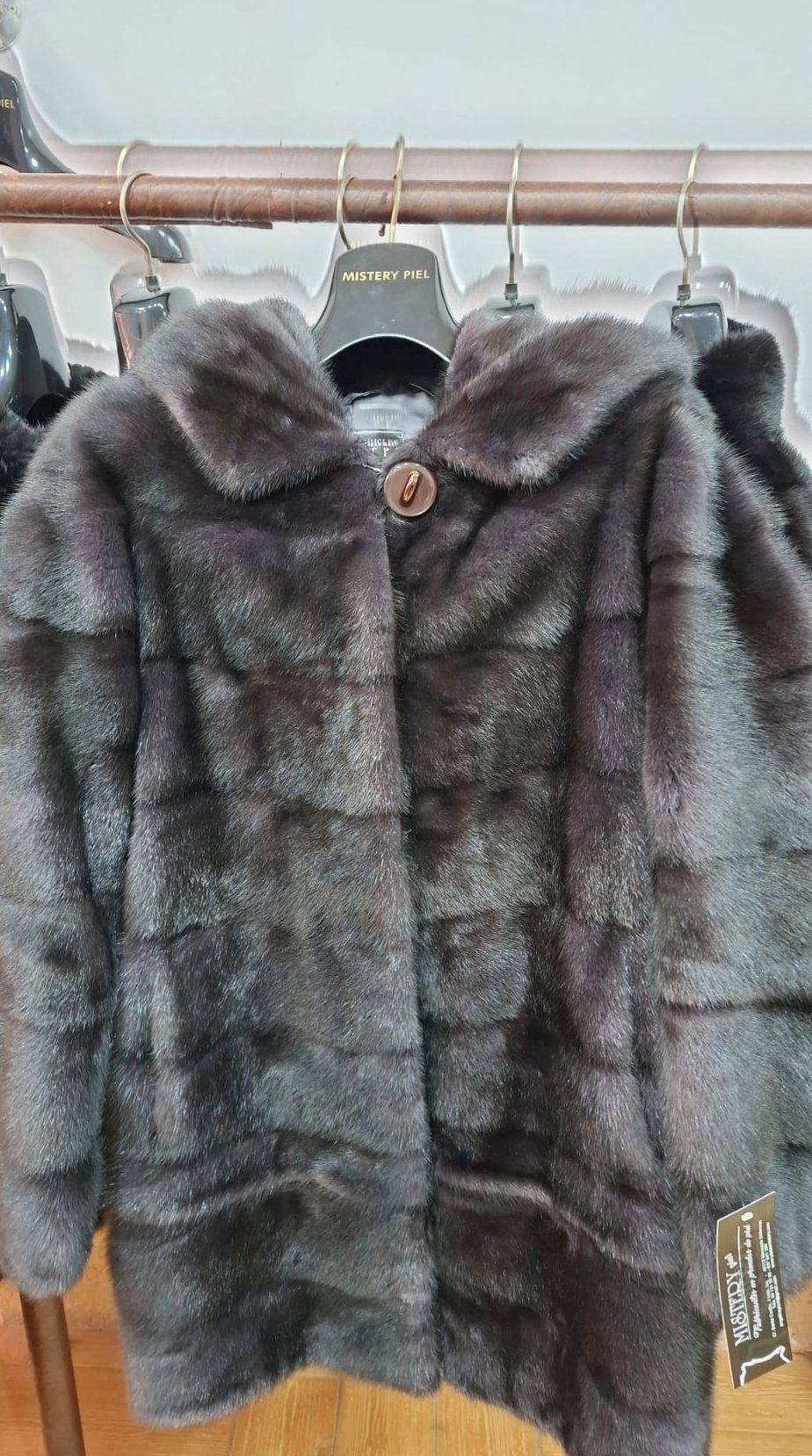 Abrigo de piel de color marrón oscuro con capucha y botón grande, colgado en un perchero.