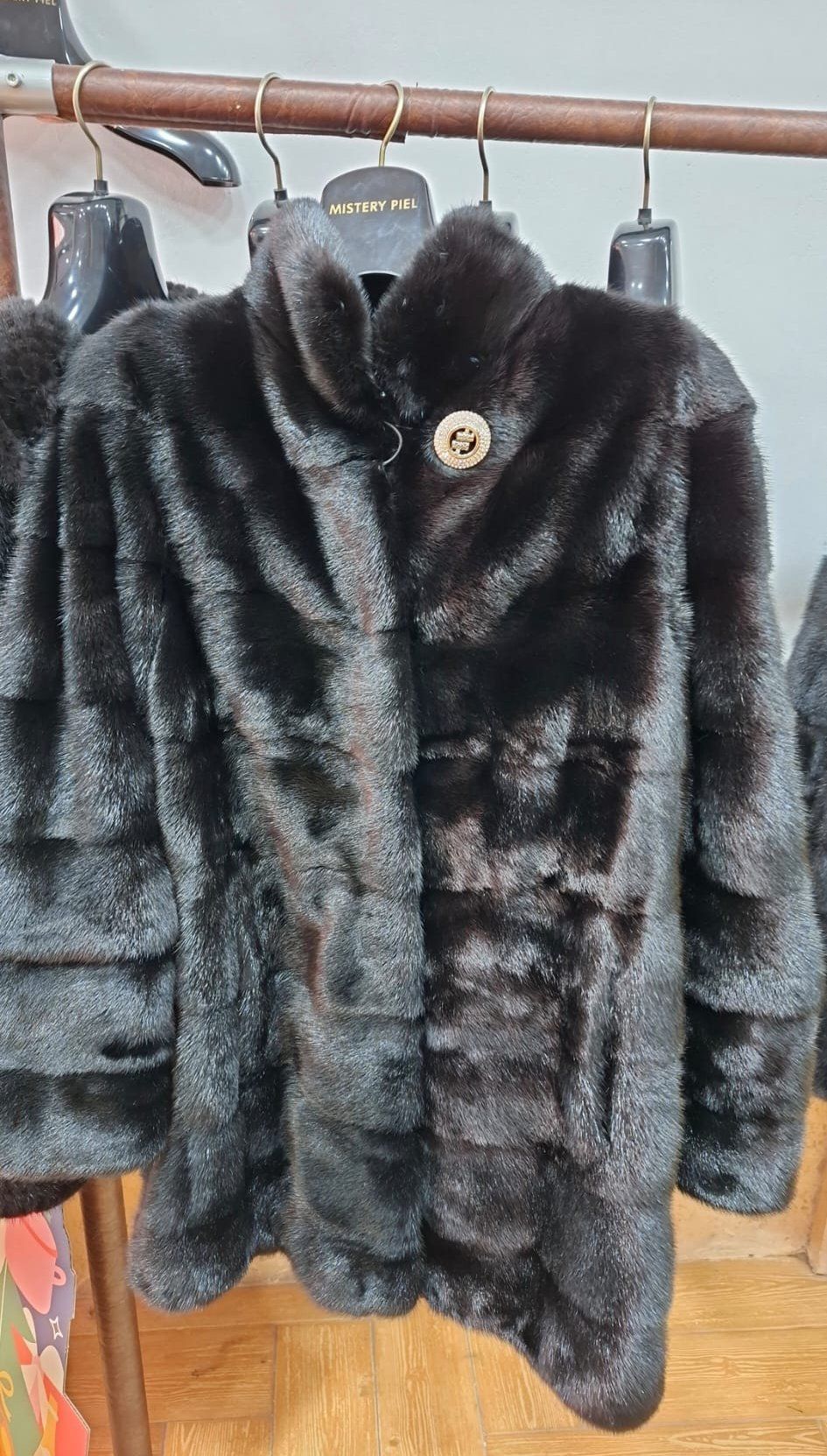 Abrigo de piel negro en percha con cierre de botón dorado.