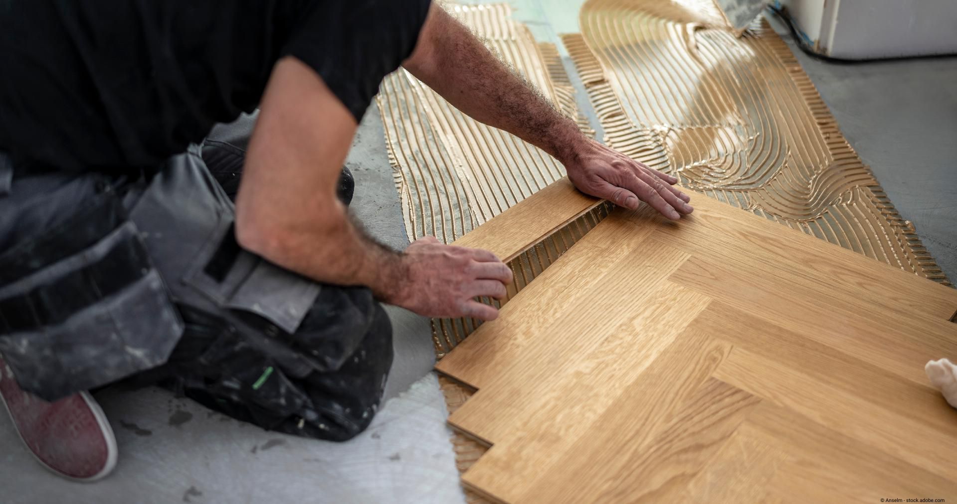 Handwerker verlegt Parkettboden mit Holzkleber