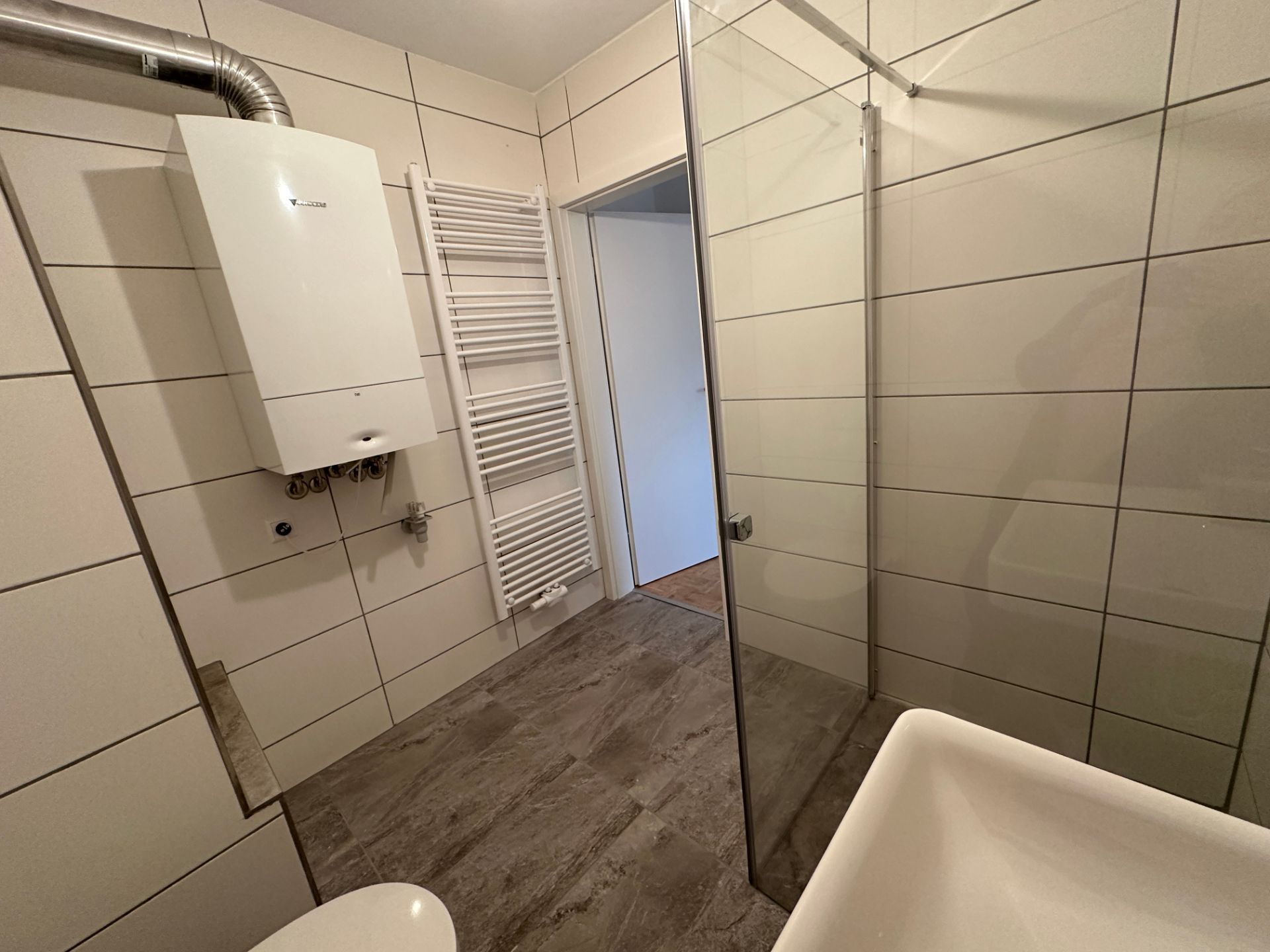 Modernes Badezimmer mit Glasdusche und hellen Fliesen in Betonoptik