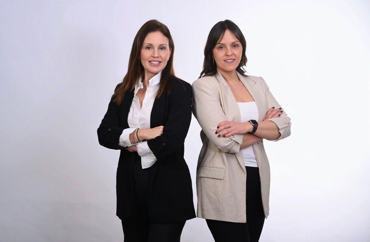Dos profesionales de pie de espaldas con los brazos cruzados sobre un fondo blanco liso.