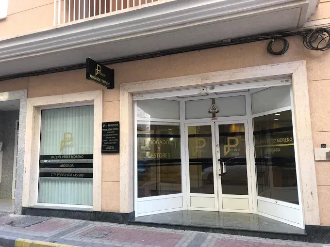 Entrada principal con puertas dobles blancas y grandes ventanales bajo un letrero negro en un edificio color melocotón.