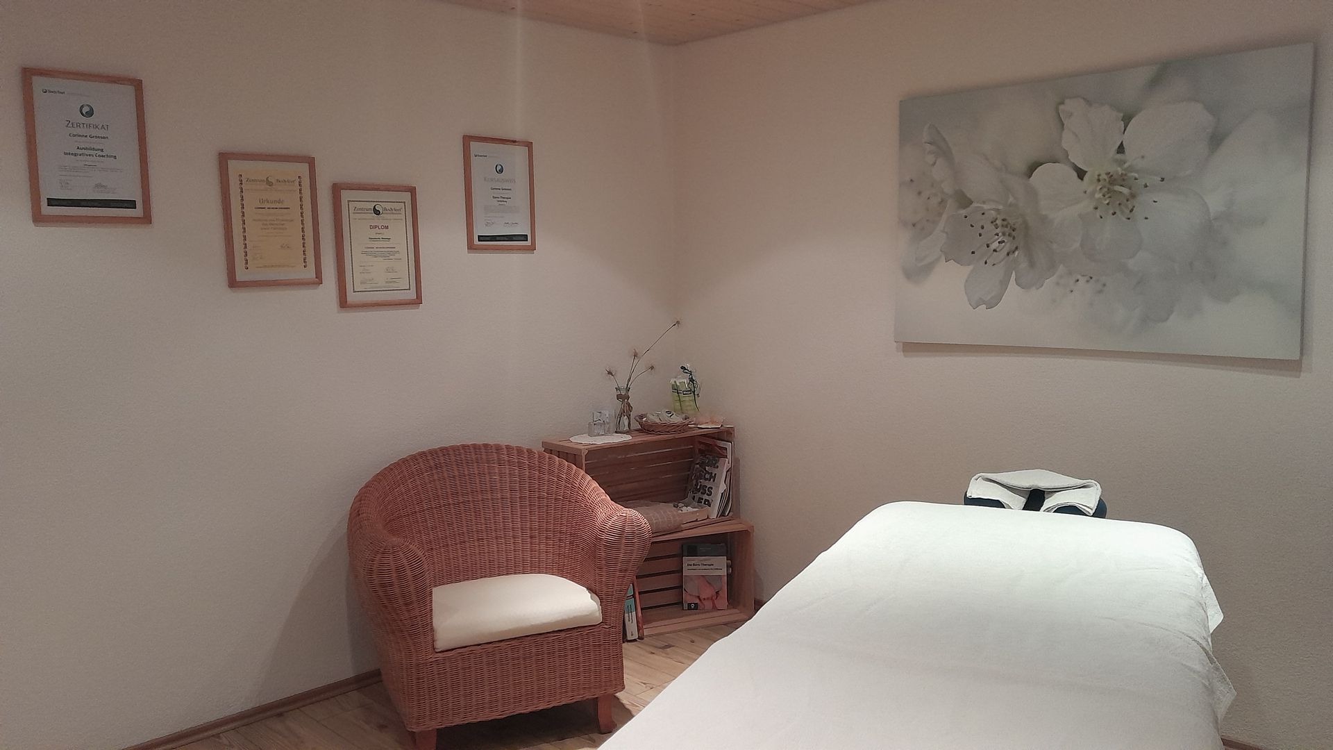 Ein Massagetisch in einem Raum mit einem Stuhl und einem Gemälde an der Wand.