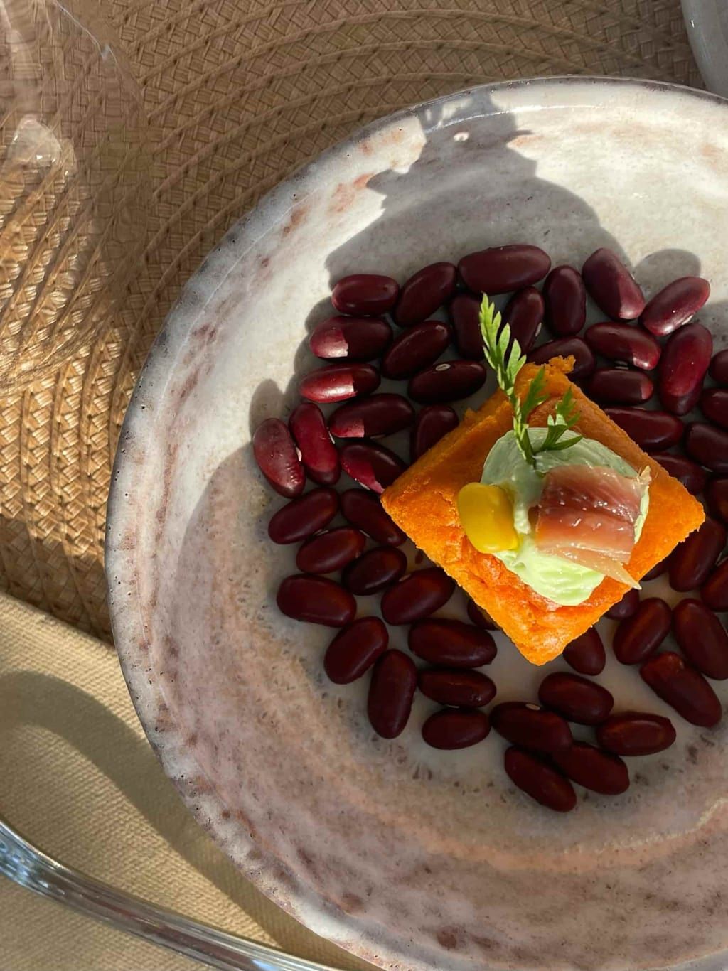 Un plato con frijoles que rodea un cuadrado de comida cubierto con una pasta verde y higos.