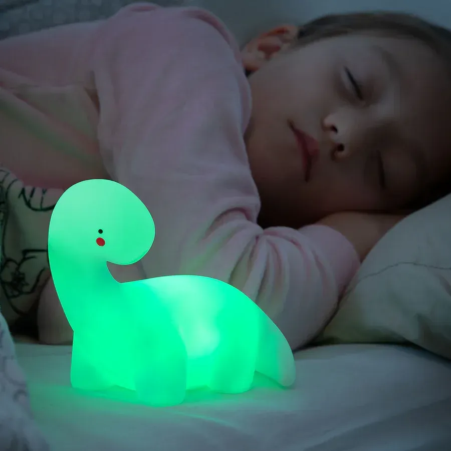 Una niña duerme junto a una lámpara de dinosaurio verde.