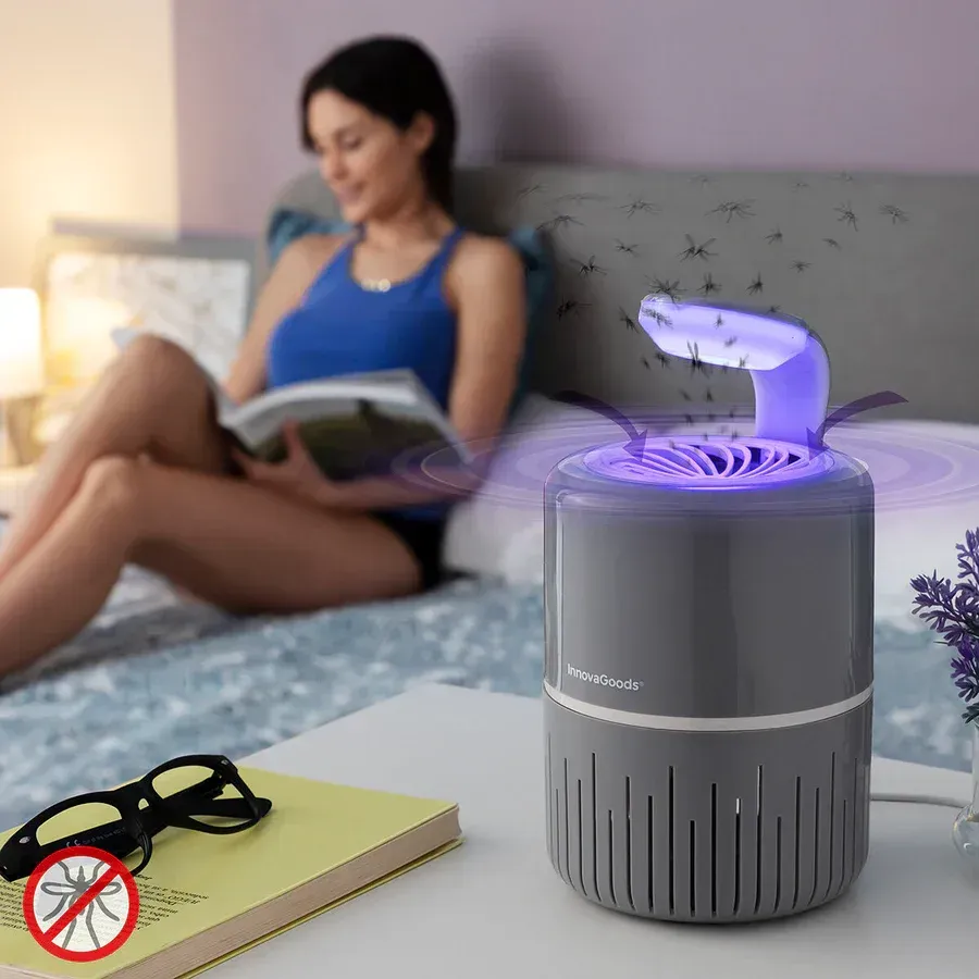 Una mujer está sentada en una cama leyendo un libro al lado de un matamosquitos.