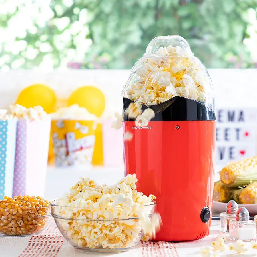 Una máquina para hacer palomitas de maíz de color rojo está sobre una mesa al lado de un tazón de palomitas de maíz.