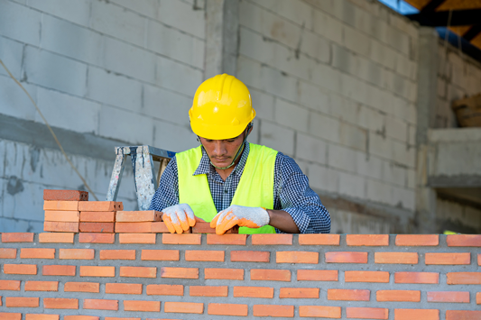 Un homme avec un casque jaune installe des briques sur un mur