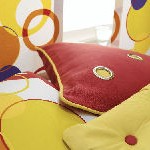 Una almohada roja está encima de una cama al lado de una almohada amarilla.