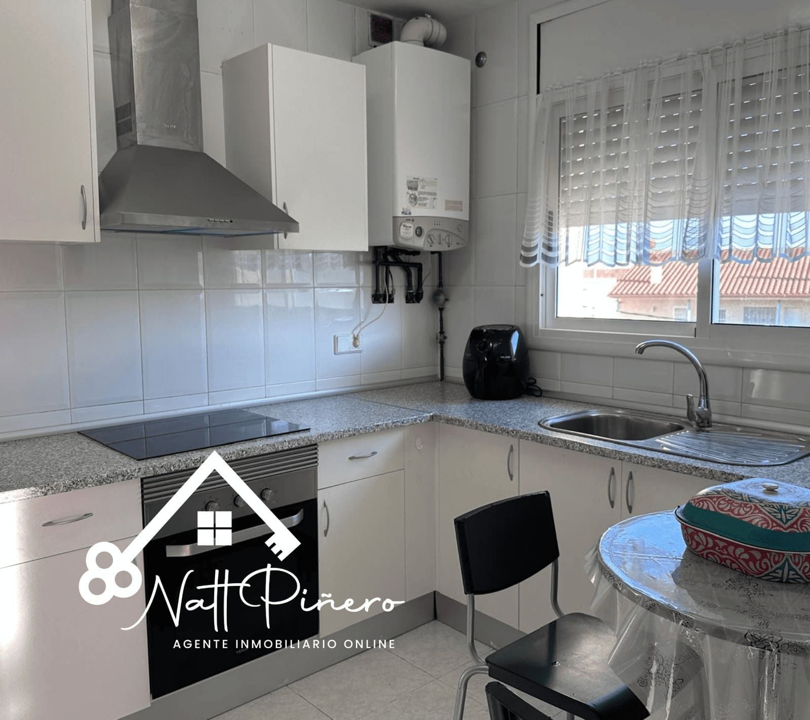 Cocina con gabinetes blancos, electrodomésticos plateados y una ventana.