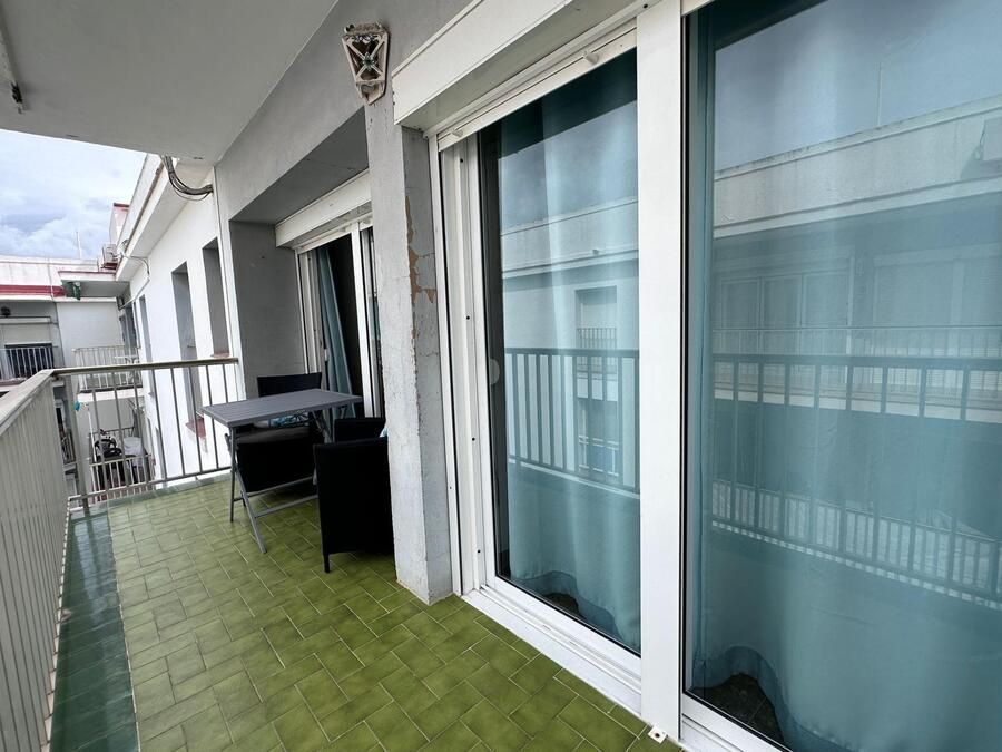 Balcón con suelo verde, mesa, sillas y puertas corredizas de cristal. Vista del paisaje urbano a través de las ventanas.