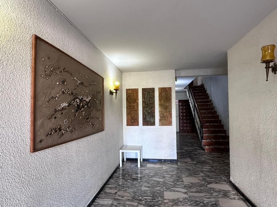 Pasillo con paredes blancas texturizadas, obras de arte, un banco blanco y una escalera.