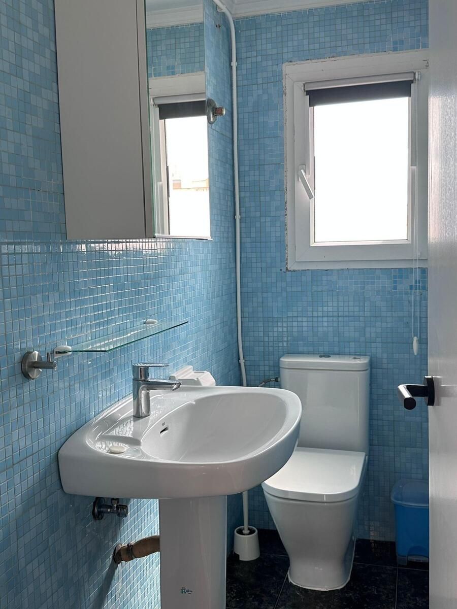 Baño con azulejos azules, lavabo, inodoro y ventana.