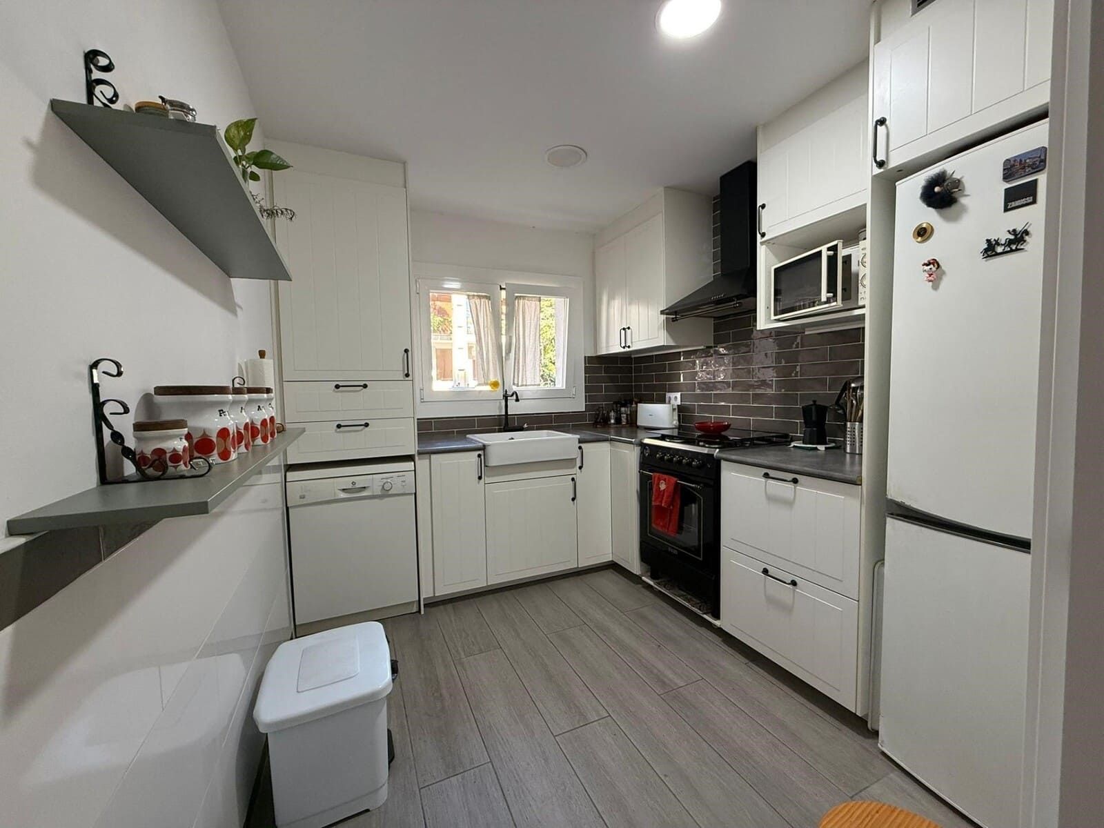 Cocina blanca con gabinetes, electrodomésticos y pisos grises.