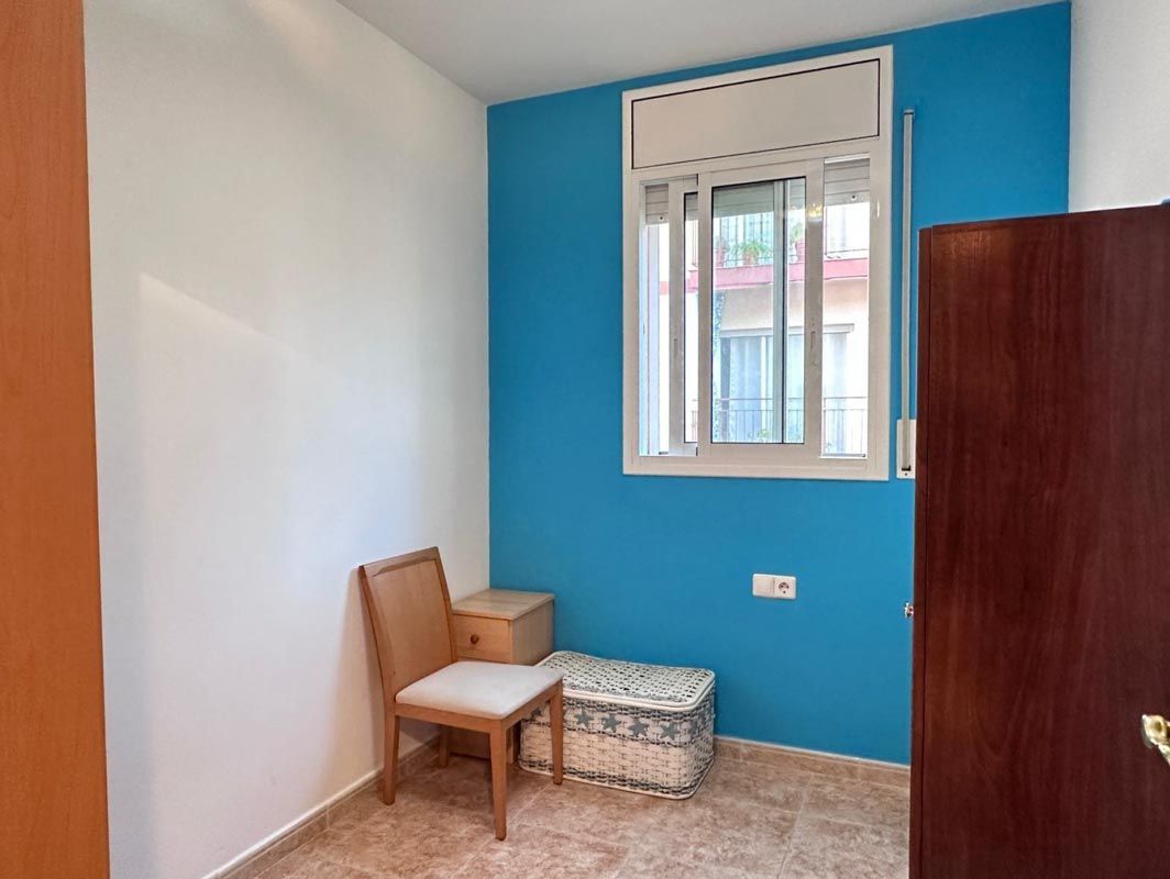Habitación pequeña con paredes azules y blancas, una ventana, una silla, espacio de almacenamiento y un armario de madera oscura.