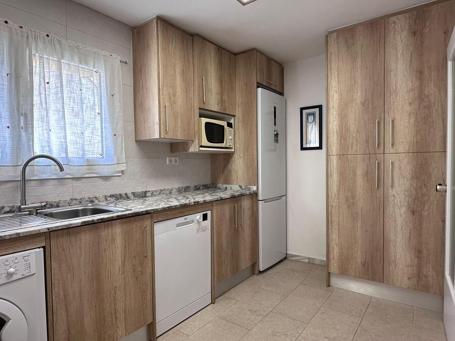 Una cocina pequeña con gabinetes de madera clara, electrodomésticos blancos y una ventana.