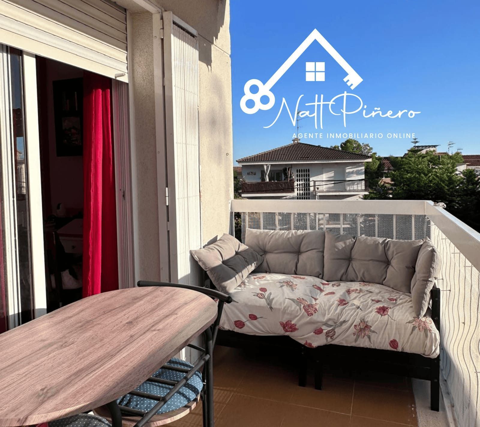 Balcón con sofá y mesa; vista de otro edificio bajo un cielo azul.