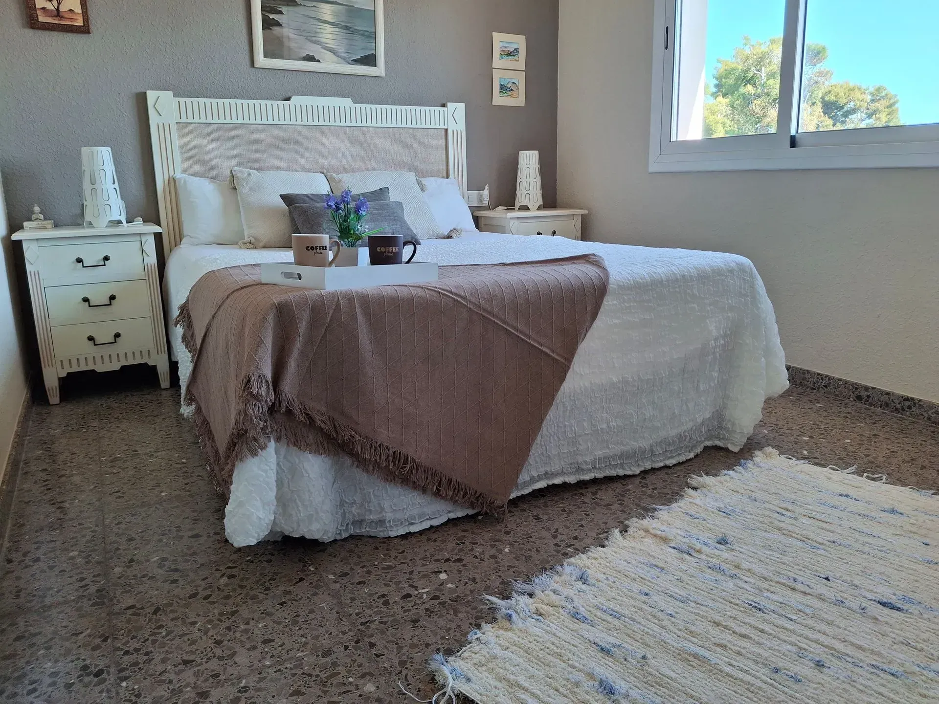 Un dormitorio con cama, mesita de noche, alfombra y ventana.