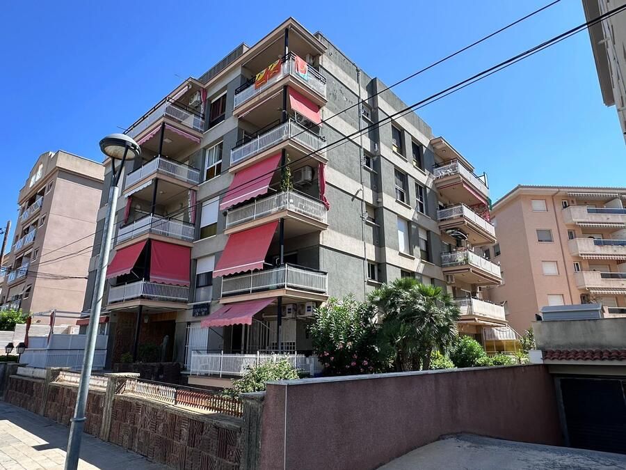 Edificio de apartamentos de varios pisos con balcones, toldos rojos y cielo azul.