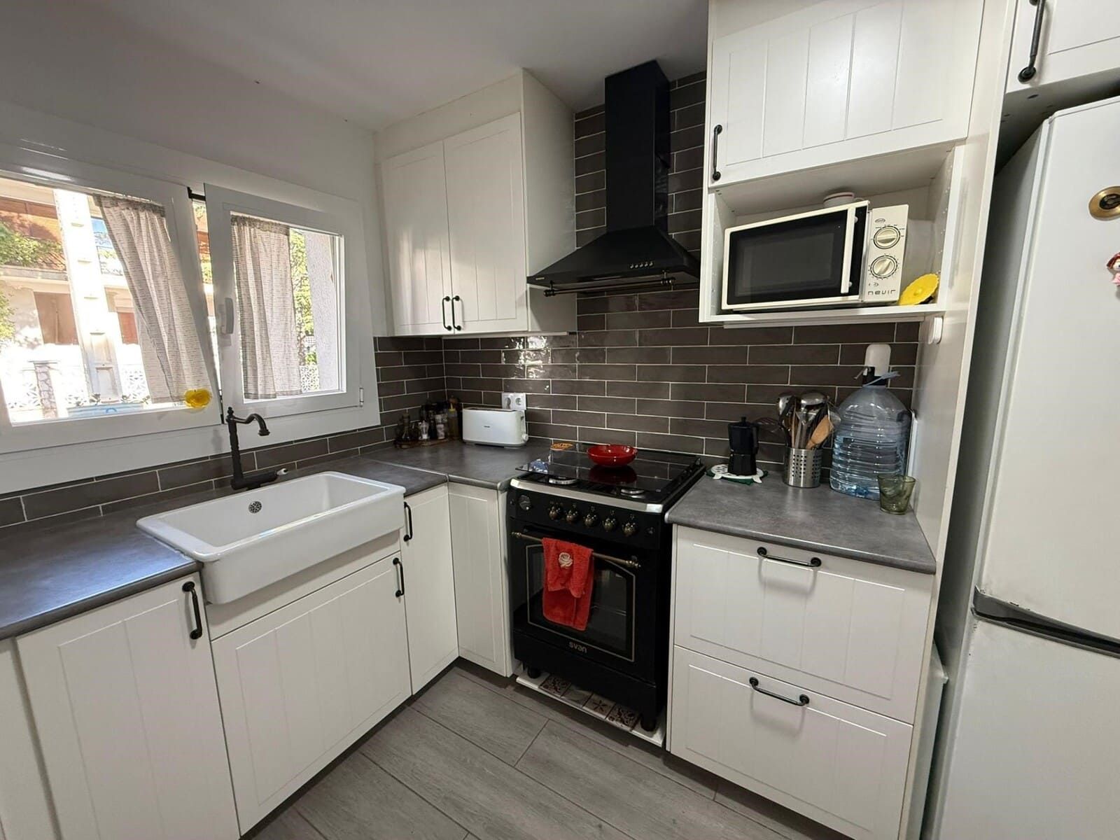 Una cocina moderna con gabinetes blancos, encimeras grises, una estufa negra y un microondas.