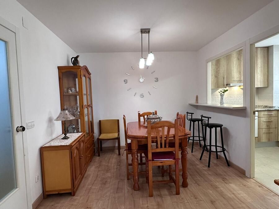 Comedor con muebles de madera, un gran reloj y un mostrador con taburetes de bar.