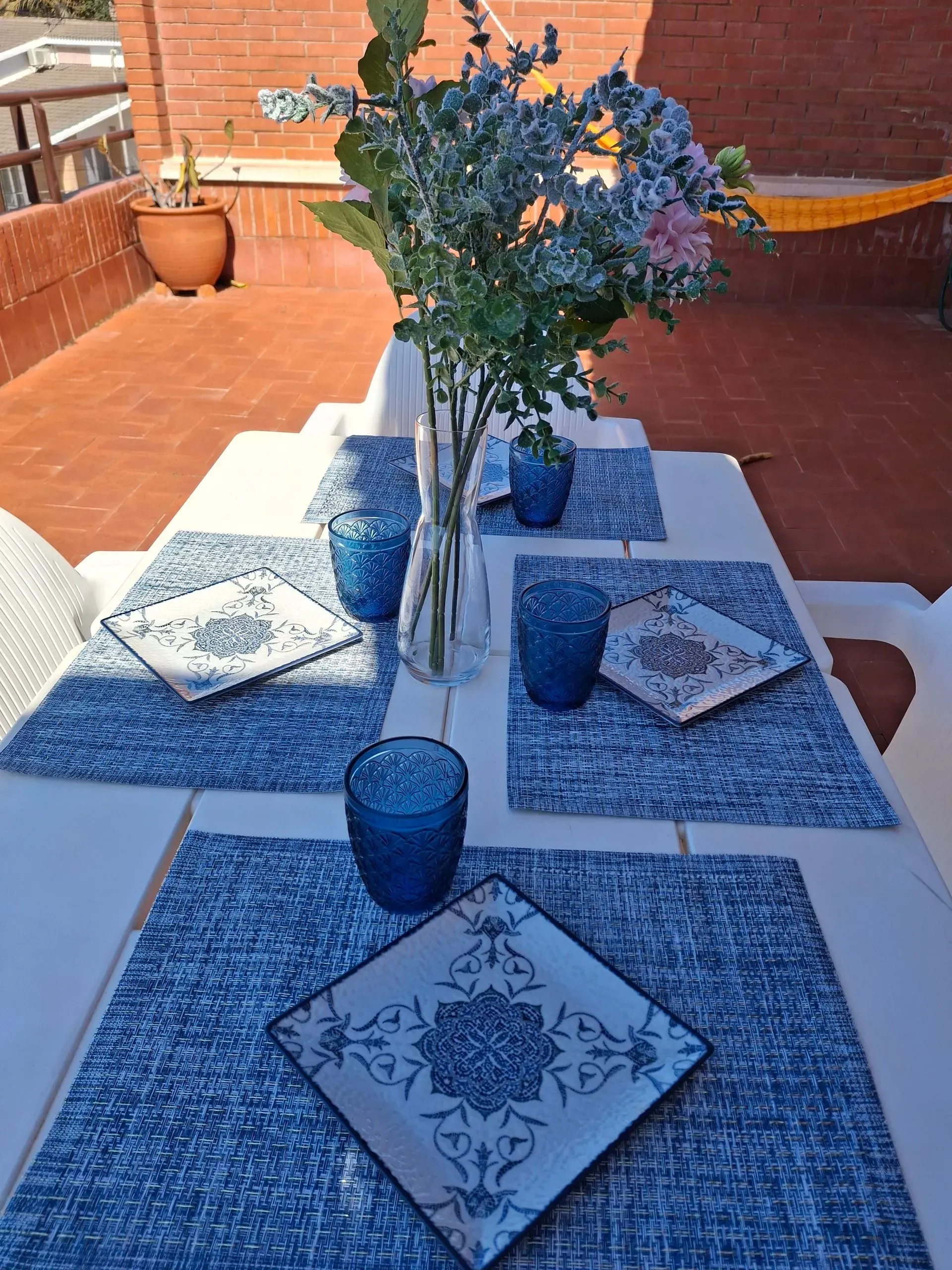 Una mesa con platos, vasos y un jarrón con flores encima.
