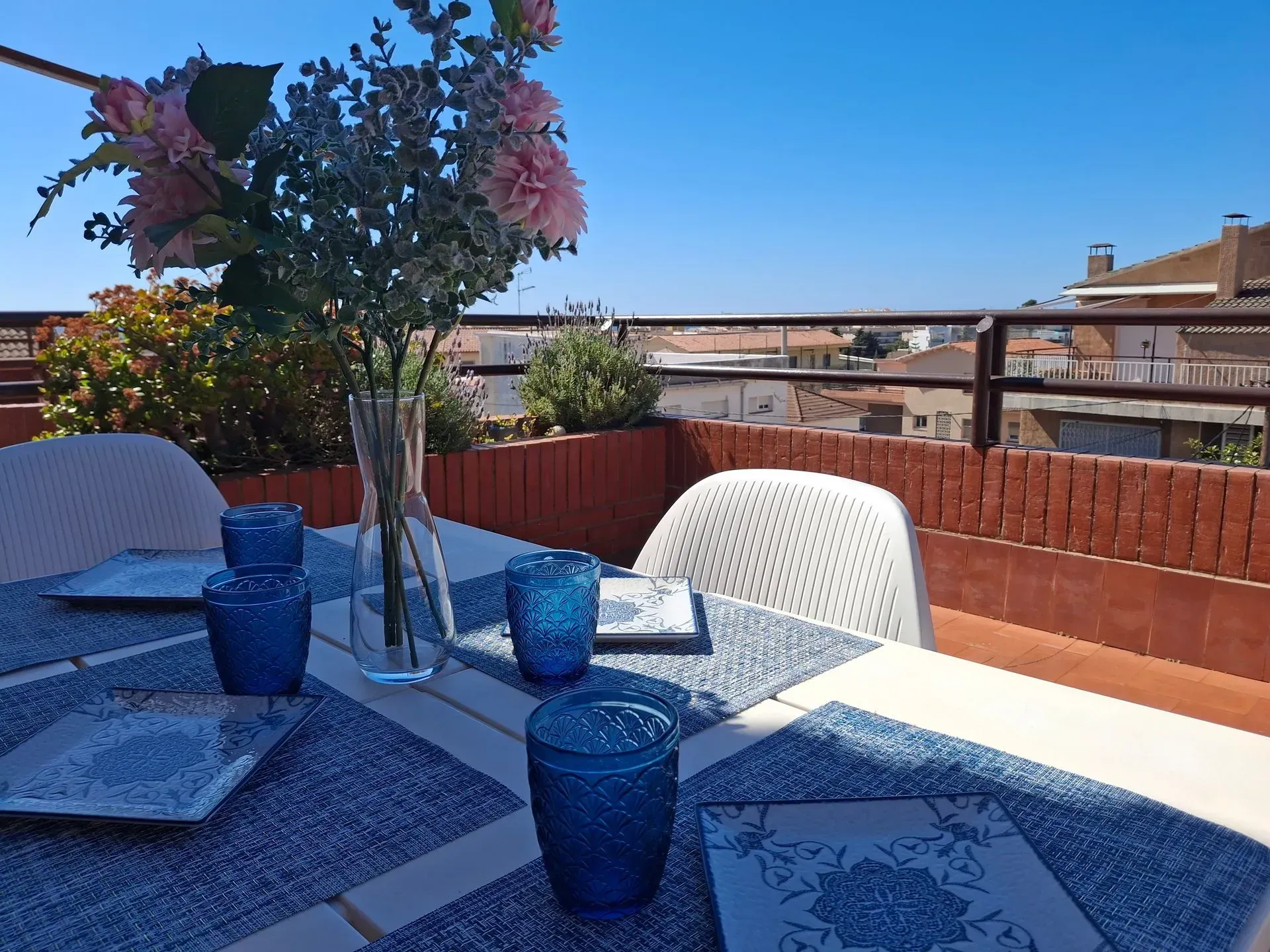 Una mesa con vasos azules y un jarrón de flores encima.
