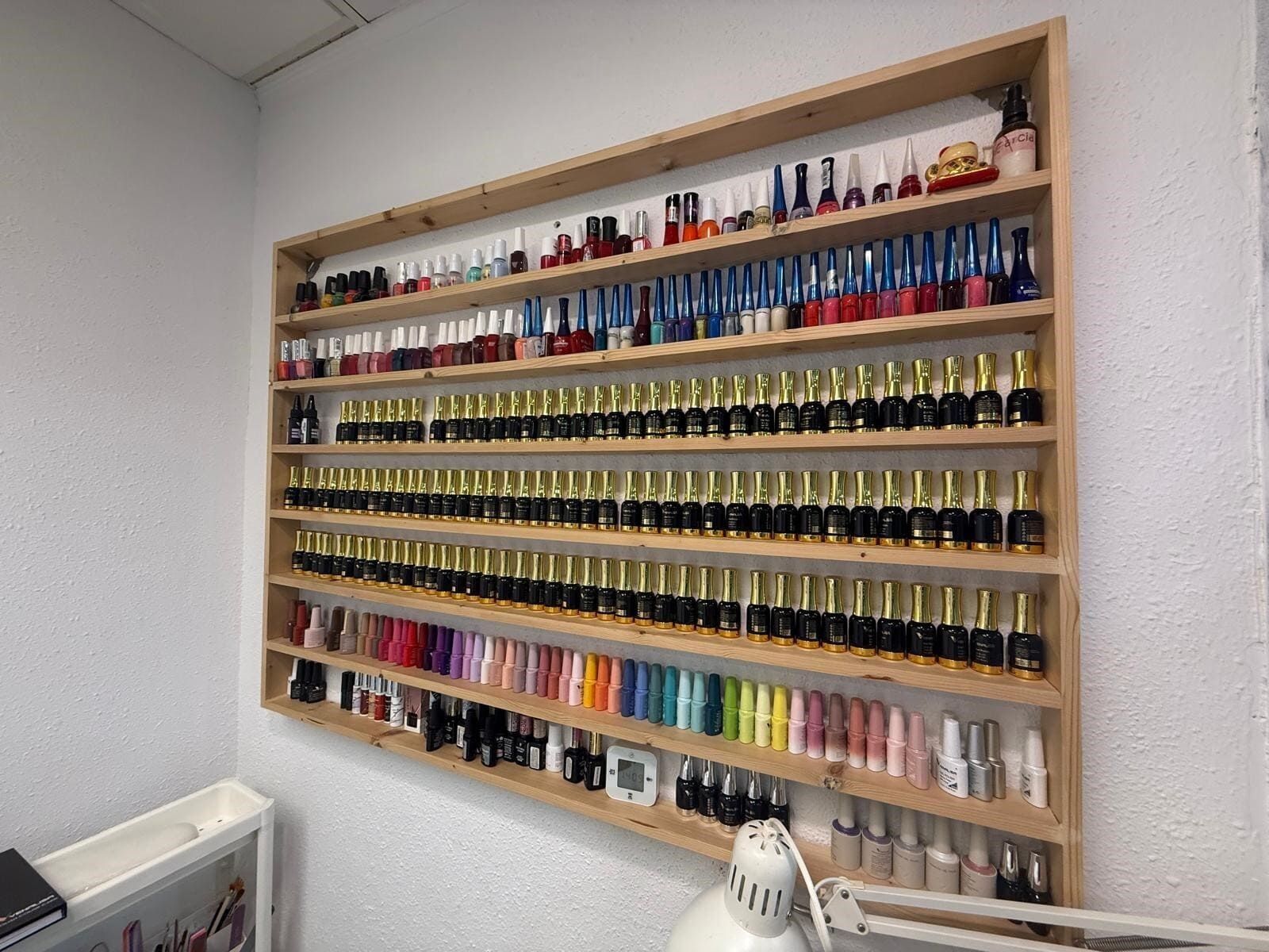 Botellas de esmalte de uñas exhibidas en estantes de madera contra una pared blanca texturizada en un salón.