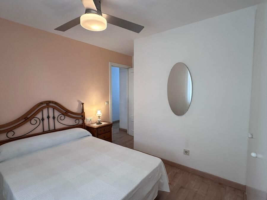 Dormitorio con cama, mesita de noche, espejo ovalado y ventilador de techo; paredes rosas y blancas.