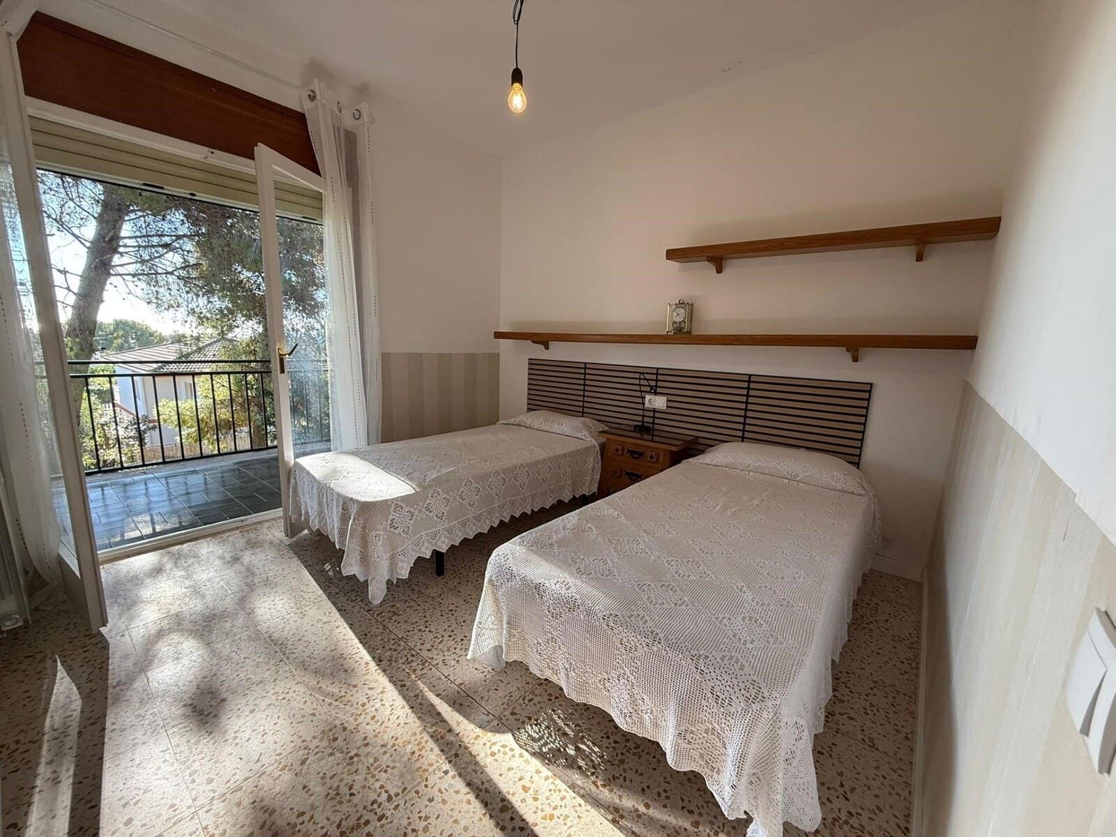 Dos camas individuales en una habitación luminosa con acceso al balcón y la luz del sol entra a raudales.