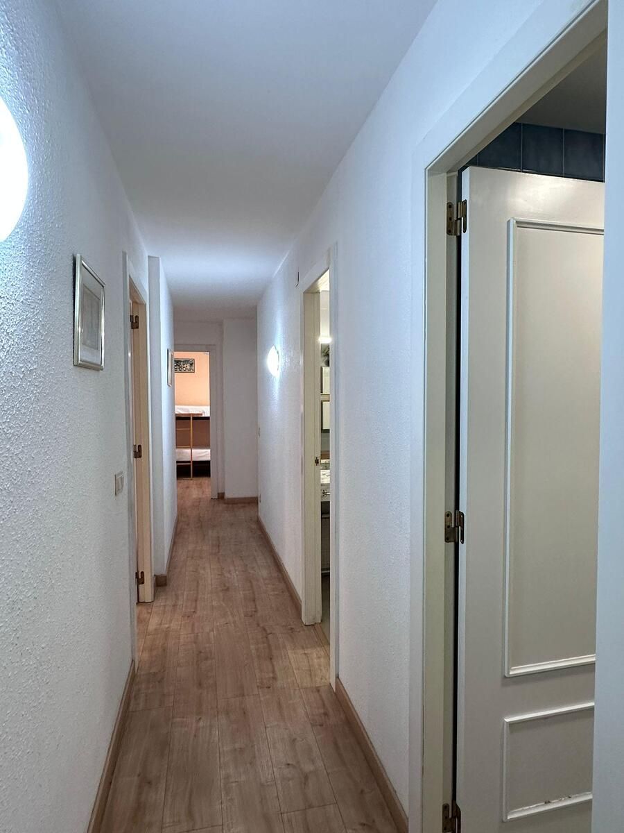 Pasillo largo y estrecho con paredes blancas, piso de madera y puertas a ambos lados.